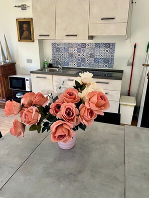 A kitchen with light-colored cabinets, a patterned backsplash, and a vase of artificial roses on a table.