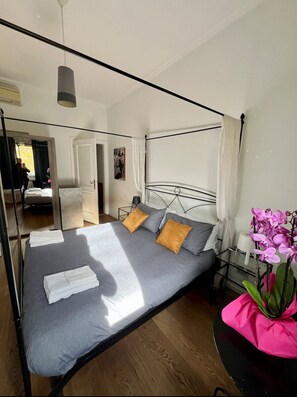 A modern bedroom with a metal frame bed, grey bedding, and a small bedside table with a lamp.