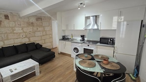 A compact living space with a sofa, a coffee table, a dining table with placemats, a washing machine, a microwave, and a refrigerator. - Renovated, two-room flat with air-conditioned, Vernet district, in city centre (Avignon)
