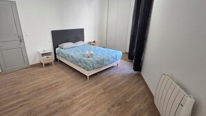 A bedroom with a bed, a nightstand, a small table, and a radiator. - Renovated, two-room flat with air-conditioned, Vernet district, in city centre (Avignon)