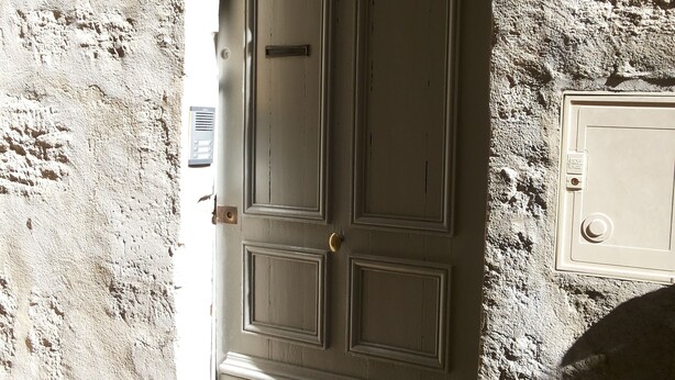 A closed door with a rectangular panel design, set in a textured wall. - Renovated, two-room flat with air-conditioned, Vernet district, in city centre (Avignon)