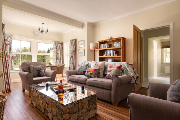 A cozy living room with a stone coffee table, a sofa with colorful cushions, a bookshelf, and a door leading to another room. - Spacious cottage on an estate where peace, privacy, fun and exploration abound (Kirkcudbright)