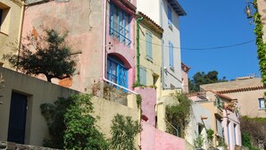 A multi-story building with balconies, a visible door, and a clear blue sky.