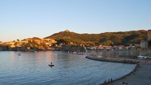A coastal town with a beach, boats, and a hill with buildings.