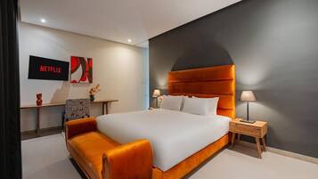 Une chambre d’hôtel moderne avec un grand lit, une table de chevet, un téléviseur et une œuvre d’art accrochée au mur.