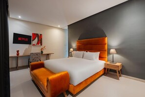 Une chambre d’hôtel moderne avec un grand lit, une table de chevet, un téléviseur et une œuvre d’art accrochée au mur.