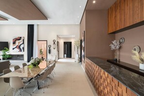 A modern dining area with a long table and chairs, a kitchen with a wooden countertop, and a hallway leading to another room.