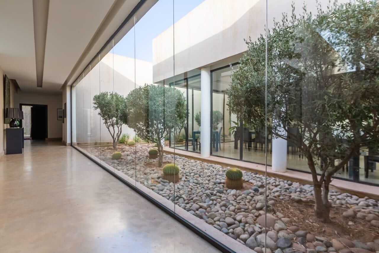 Edifici modern amb façana de vidre, passeig pavimentat i un petit jardí amb cactus i arbres.