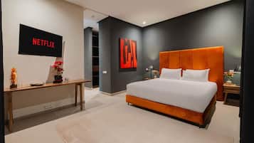 A modern bedroom with a large bed, a TV mounted on the wall, and a desk with a vase of flowers.