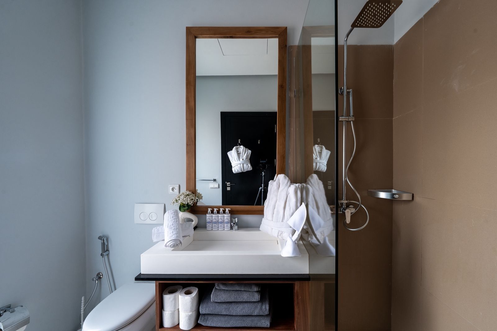 Ein modernes Badezimmer mit großem Spiegel, Dusche, Toilette und Waschtisch mit Handtüchern und Pflegeprodukten.