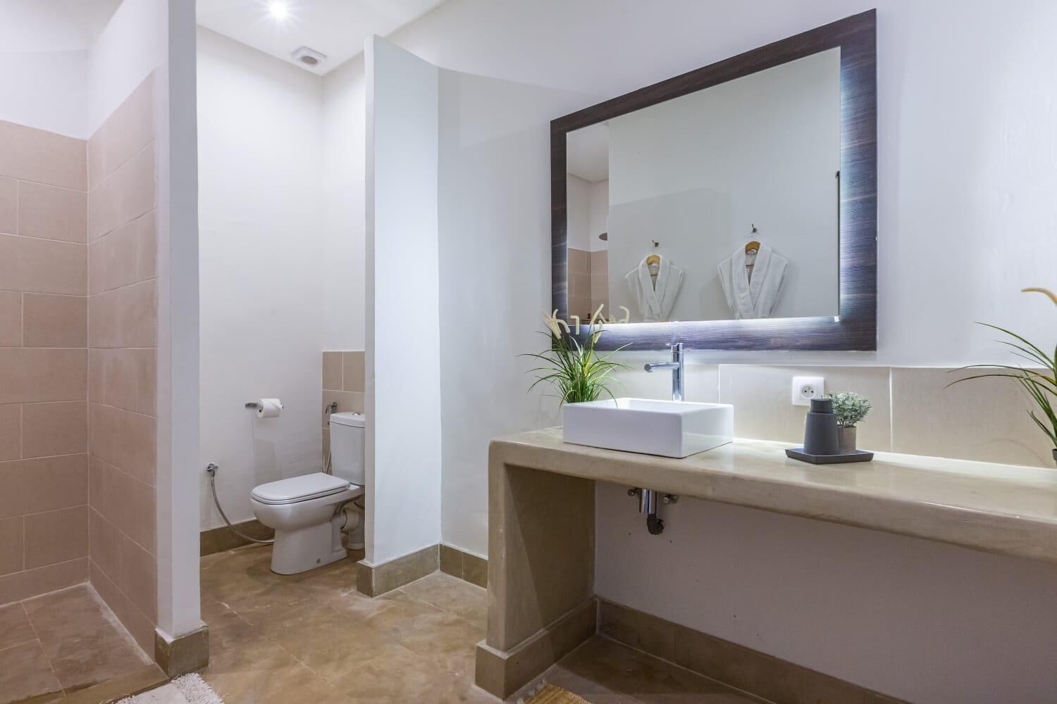 Ein modernes Badezimmer mit einem weißen Waschbecken, einem großen Spiegel und einer Toilette.