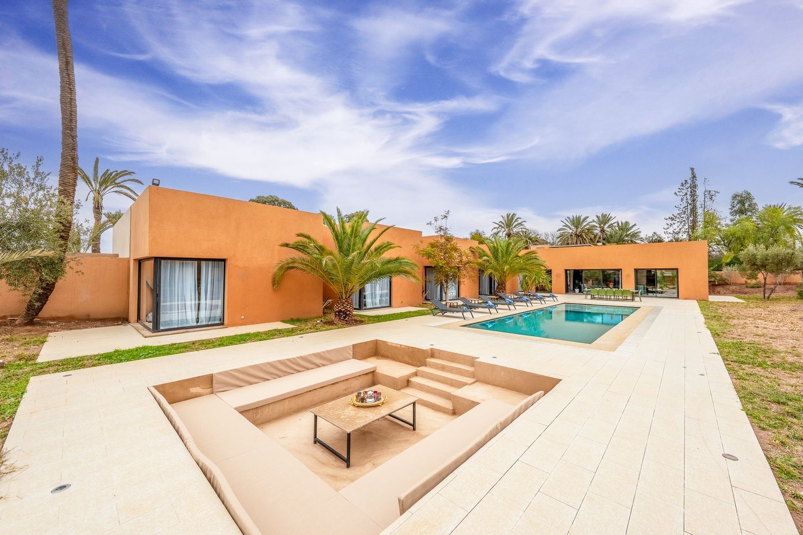 A modern outdoor pool area with a built-in seating area and palm trees.