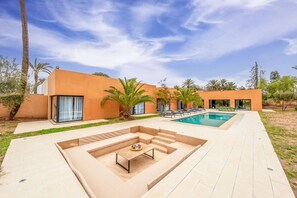 A modern outdoor pool area with a built-in seating area and palm trees. - Villa 865 + (Marrakech)