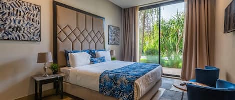 A hotel room with a large bed, a desk, two chairs, and a view of greenery.