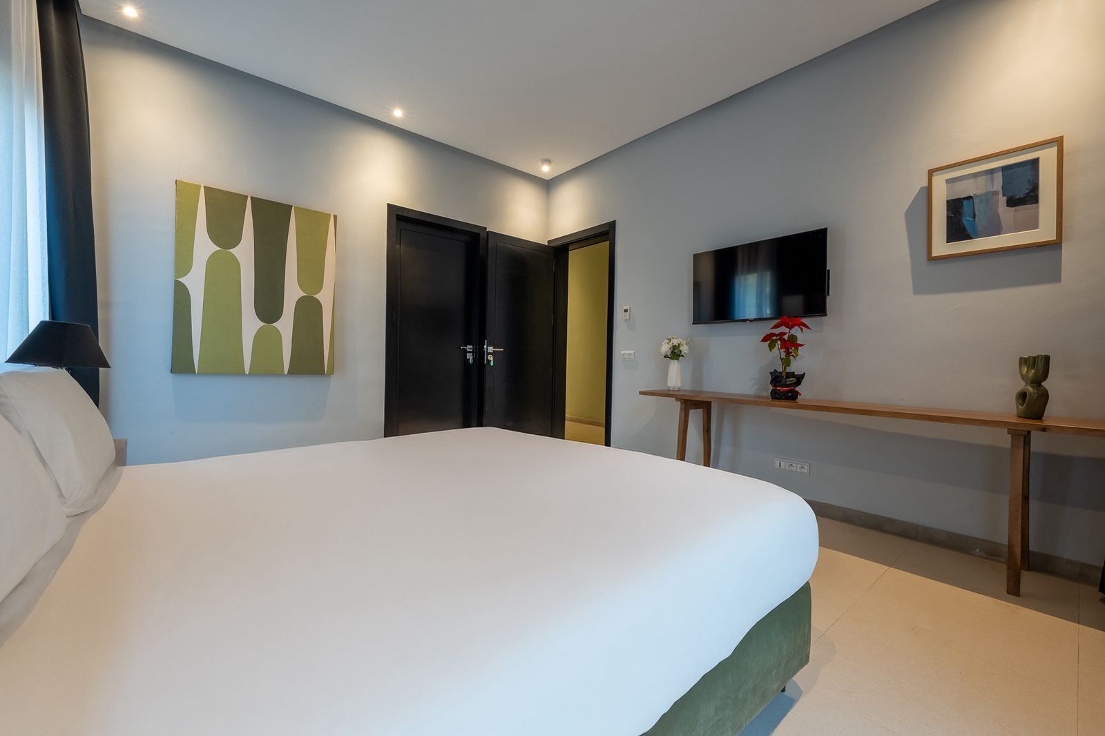Une chambre d’hôtel avec un grand lit, un bureau agrémenté d’un vase, un téléviseur à écran plat et un tableau au mur.