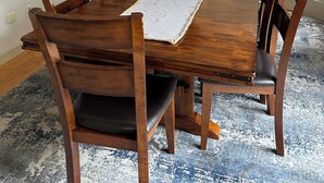 Une salle à manger avec une table en bois, des chaises, un vase de fleurs et un tableau au mur.