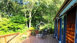 Une terrasse en bois avec une balustrade, une petite table et des chaises, et une vue sur une zone boisée.