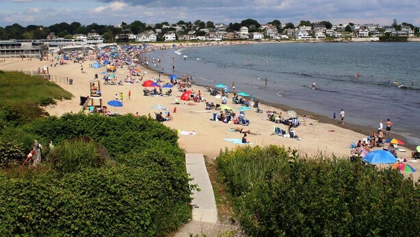 Une plage avec des gens, des parasols et des maisons en arrière-plan.