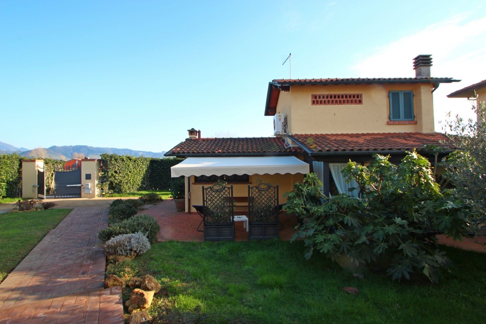 A two-story house with a tiled roof, a covered patio, and a garden with a paved walkway.