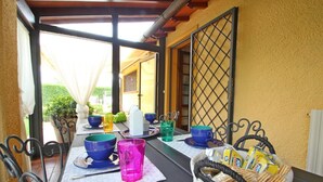 Un espace de restauration en plein air avec des chaises et des tables en métal, un panier de pain, ainsi que différentes tasses et bols de couleurs variées.