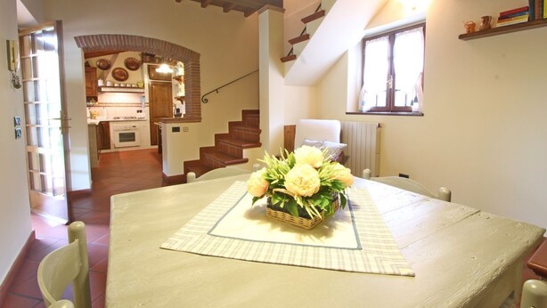 Un coin repas avec une table dressée pour deux personnes, un escalier et une cuisine en arrière-plan.
