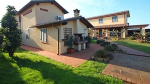 Une maison à deux étages avec une terrasse en briques, un petit jardin et une cheminée.