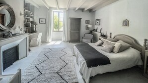 Une chambre à coucher avec un lit, une chaise, un bureau, une cheminée et une fenêtre.