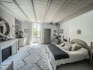 Een slaapkamer met een bed, een stoel, een bureau, een open haard en een raam.