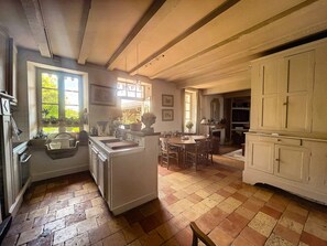 Een ruime keuken met een groot eiland, houten kastjes en een eethoek met een open haard.