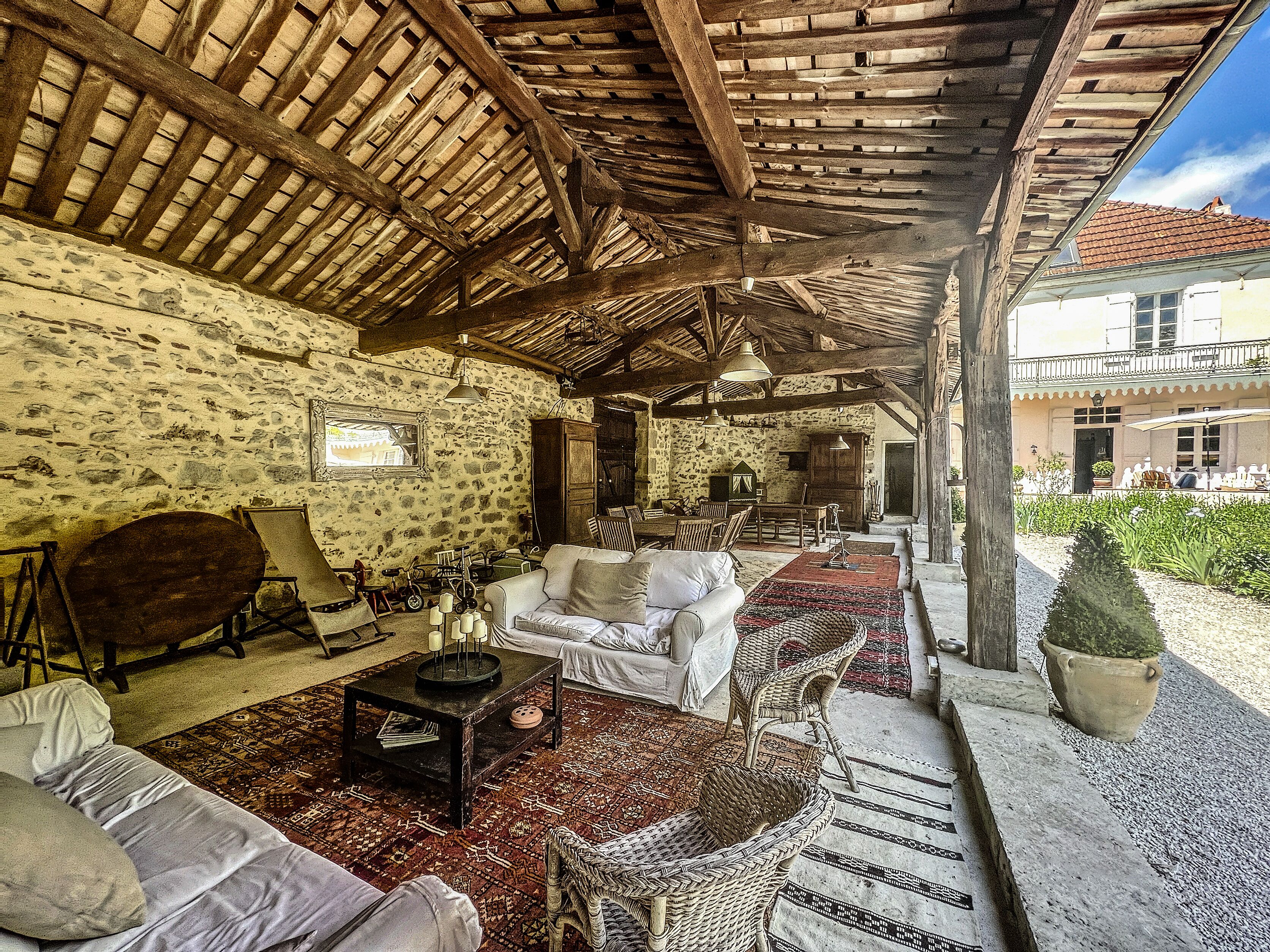 A rustic interior with stone walls, wooden beams, a stone fireplace, and a dining area with outdoor seating.