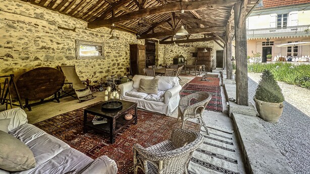 Un intérieur rustique avec des murs en pierre, des poutres en bois, une cheminée en pierre et un coin repas avec des sièges à l’extérieur.