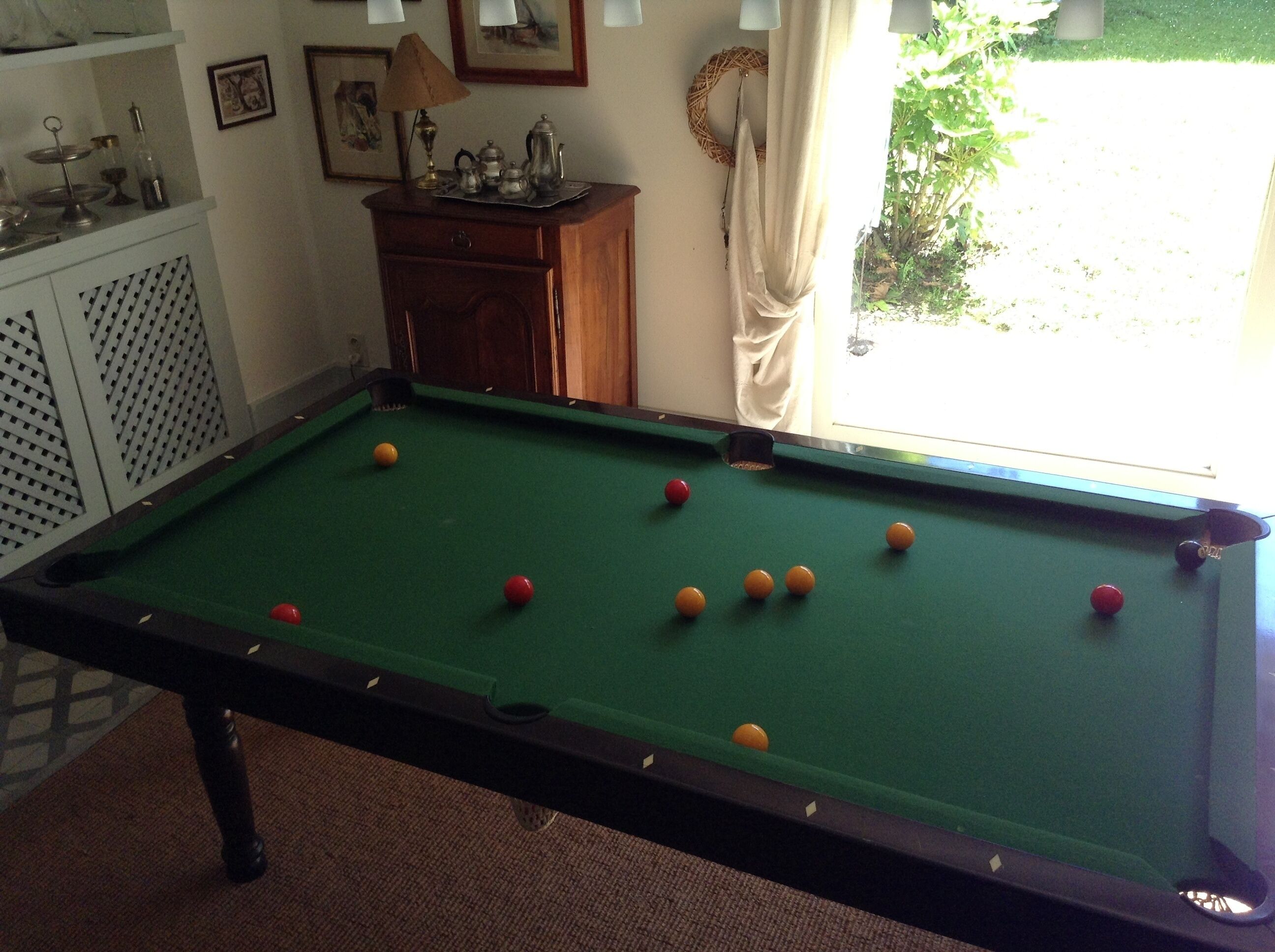 Une table de billard avec des billes, une lampe et un meuble contenant des objets décoratifs.