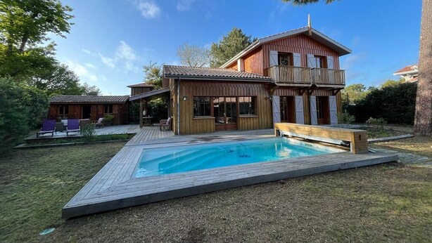 Ein zweistöckiges Holzhaus mit Swimmingpool, Terrasse und Sitzbereich im Freien.