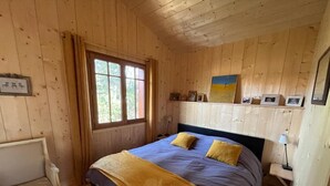 Ein Schlafzimmer einer Holzhütte mit einem Bett, einem Nachttisch, einer Lampe und einem Fenster.