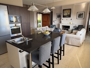 Una cocina moderna con una isla central, electrodomésticos de acero inoxidable y un comedor con sillas tapizadas en gris.