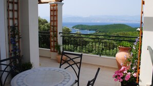 Un balcon donnant sur un paysage côtier, une plante en pot et une table avec des chaises.