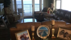 A living room with a brown leather sofa, a glass coffee table, and a fireplace. There are two framed pictures on the table. - Beautiful Daytona Ocean-Front Condo-Everything You Can Imagine (Daytona Beach Shores)