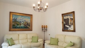 A living room with two white sofas, a chandelier, and two framed paintings on the walls.