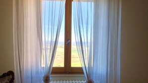A room with a window covered by sheer curtains, a radiator below, and a floral-patterned armchair to the left.