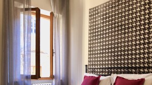 A bedroom with a bed, a radiator, a window with curtains, and a patterned wall.