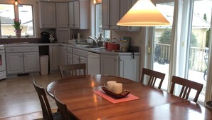 Une cuisine avec des meubles blancs, une table à manger en bois avec des chaises et un luminaire suspendu.