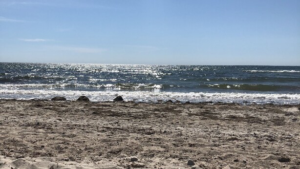 Une plage de sable avec des vagues, sous un ciel dégagé.