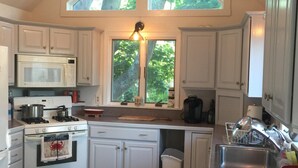 Une cuisine avec des meubles blancs, une cuisinière, un four à micro-ondes, un évier et un ventilateur de plafond.