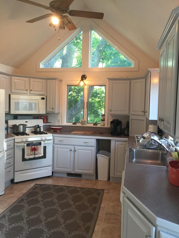A kitchen with white cabinets, a stove, a microwave, a sink, and a ceiling fan.