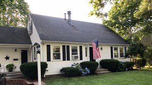 Une maison à deux étages, avec un toit sombre, un revêtement extérieur blanc et une véranda à l’avant.