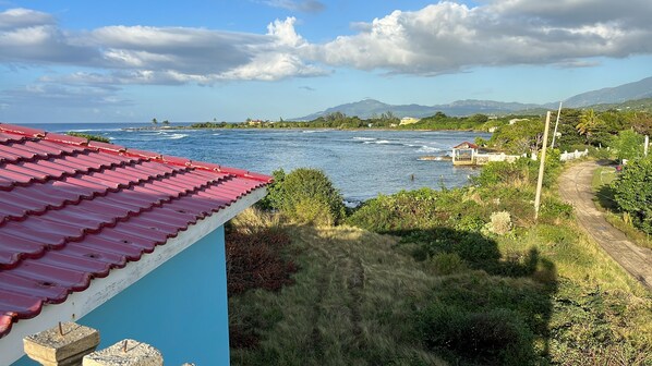 A coastal view with a red-roofed building, a clear sky, and a distant mountain range.