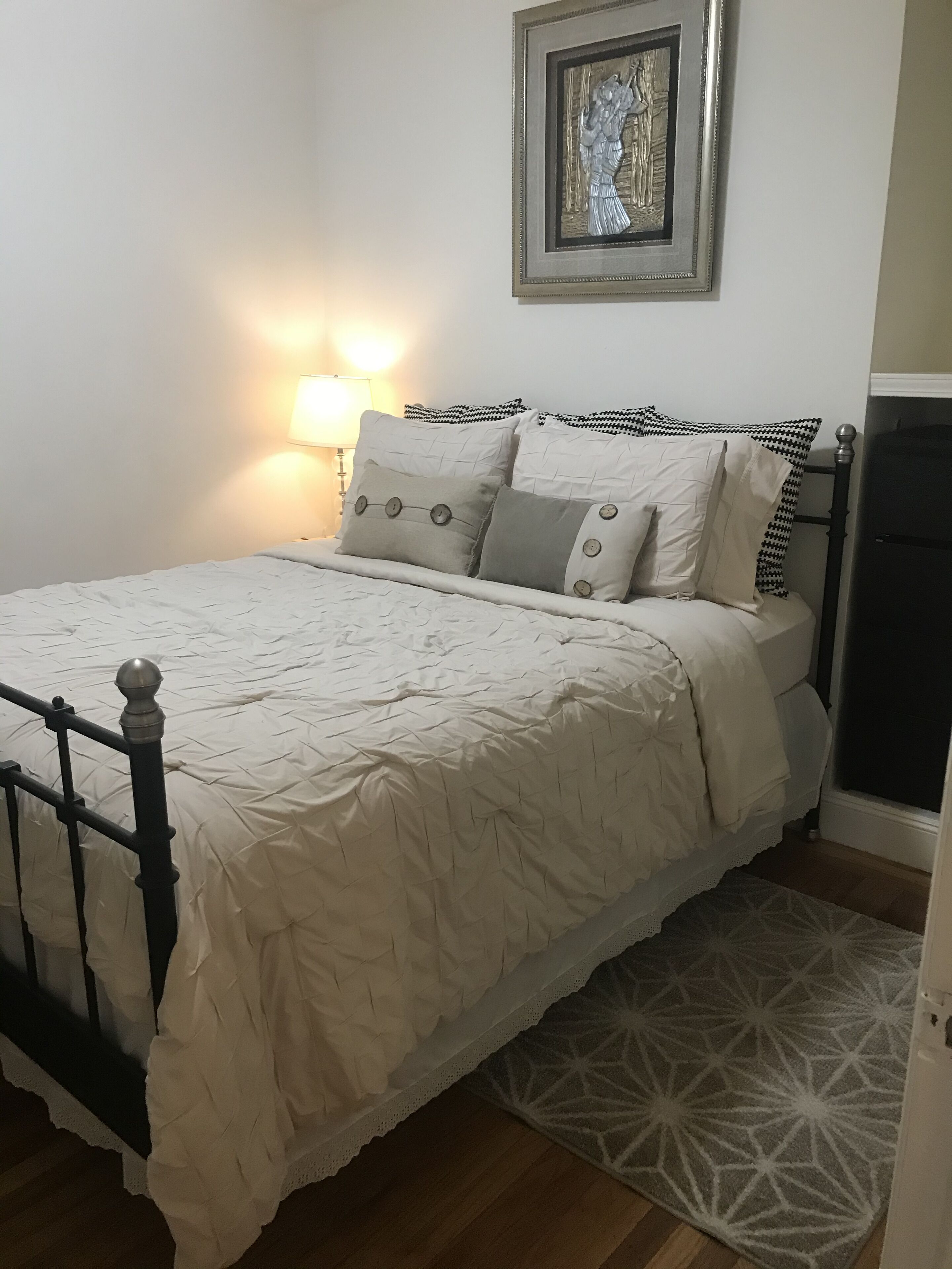 A neatly made bed with a white duvet, a black metal frame, and a patterned rug.