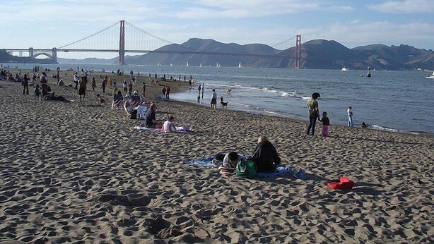 Une plage avec des gens, un pont et des bateaux en arrière-plan.