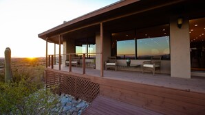 Une terrasse en bois avec des sièges extérieurs, offrant une vue sur un paysage désertique avec des cactus et un coucher de soleil.