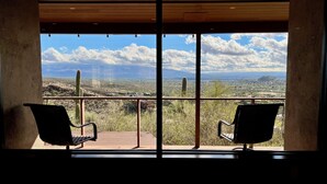 Un balcon avec deux chaises donnant sur un paysage désertique pittoresque, avec des cactus et des montagnes à l’horizon.